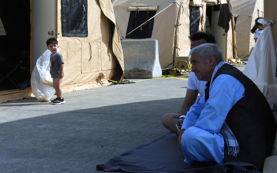Men sit in a shady spot among tents as a little boy looks around inside the temporary living area for Afghan evacuees at Ramstein Air Base, Germany, Aug. 21, 2021.

 
