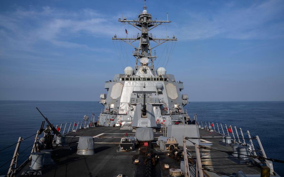 The deck of a military naval destroyer is seen from the bridge as it sails in open water, with the horizon in the background.