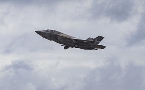 A military fighter jet ascends through a cloudy sky.