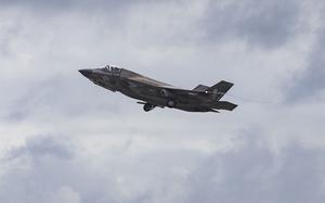 A military fighter jet ascends through a cloudy sky.