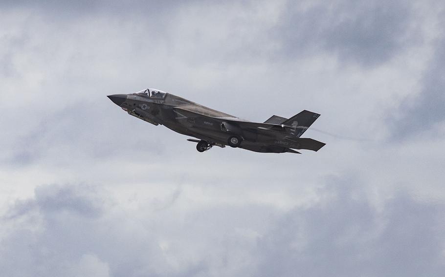 A military fighter jet ascends through a cloudy sky.