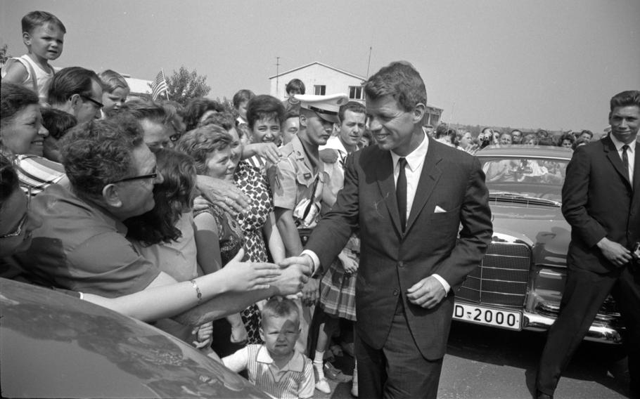 RFK shakes a woman’s hand as others near them reach their hands forward.