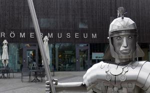 A stylized metal statue of a Roman soldier stands in front of the Roemermuseum in Osterburken, Germany. The museum features the remnants of a Roman bath and artifacts from the time when they had a fort guarding the border here.
