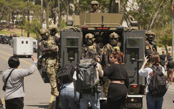 Federal agents ride on an armored vehicle as several people look on.