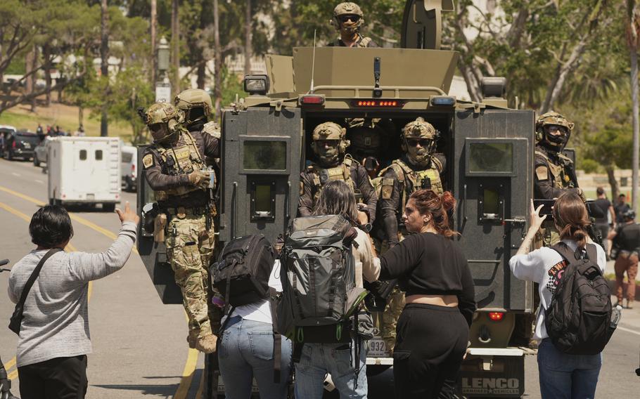 Federal agents ride on an armored vehicle as several people look on.