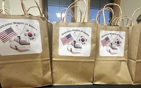 Brown paper grocery bags with white signs reading “Welcome Wagon of Korea” and pictures of U.S. and South Korean flags rest on a table.