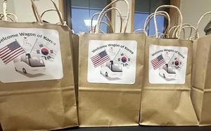 Brown paper grocery bags with white signs reading “Welcome Wagon of Korea” and pictures of U.S. and South Korean flags rest on a table.