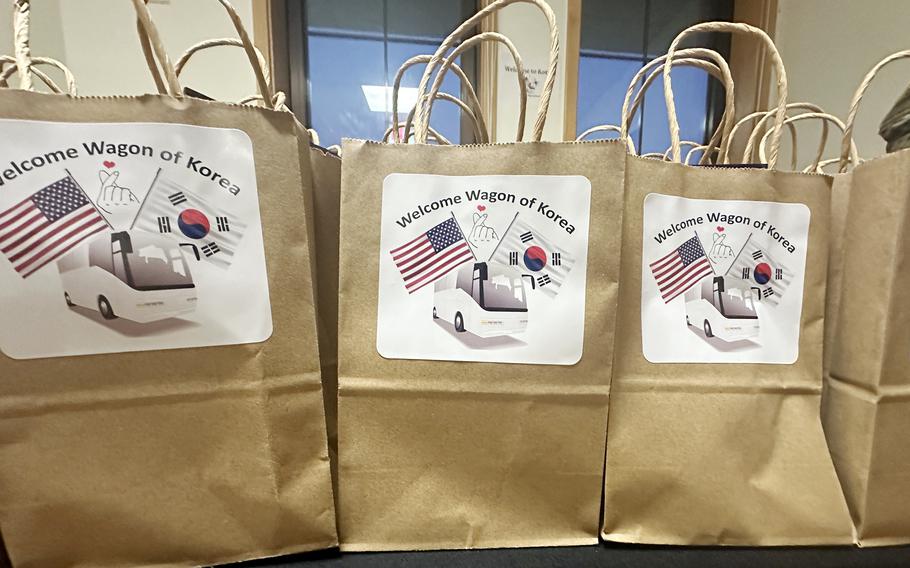 Brown paper grocery bags with white signs reading “Welcome Wagon of Korea” and pictures of U.S. and South Korean flags rest on a table.