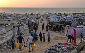 People walk by a mass of tents near a beach.