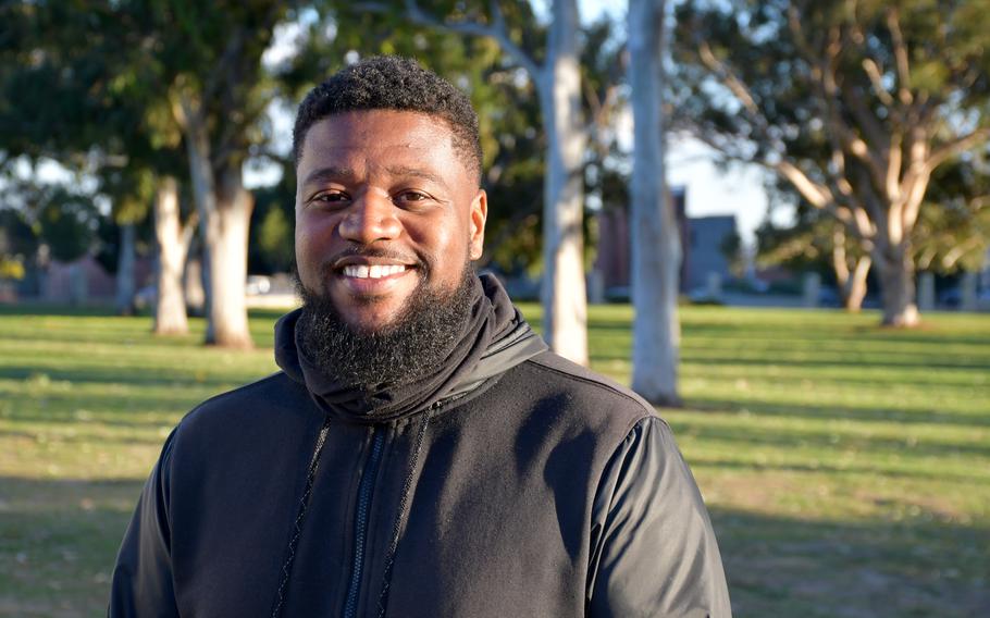 Navy veteran Kevin Huey, 34, poses on the grounds of the West Los Angeles VA campus on Wednesday, Feb. 23, 2022. Behind Huey was recently the site of Veterans Row, a homeless encampment along San Vicente Boulevard, abutting one end of the VA campus. The encampment was eliminated in November, and veterans were allowed to move onto VA grounds. Huey, who became homeless after the coronavirus pandemic upended his college plans, lives in a tiny shelter at the VA.