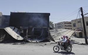 Syrian citizens on a motorbike ride past a burned-out shop.