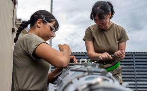 Two airmen use tools to disassemble a bomb outdoors.
