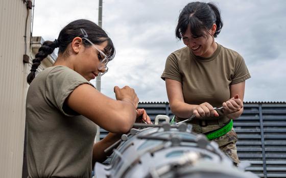 Two airmen use tools to disassemble a bomb outdoors.