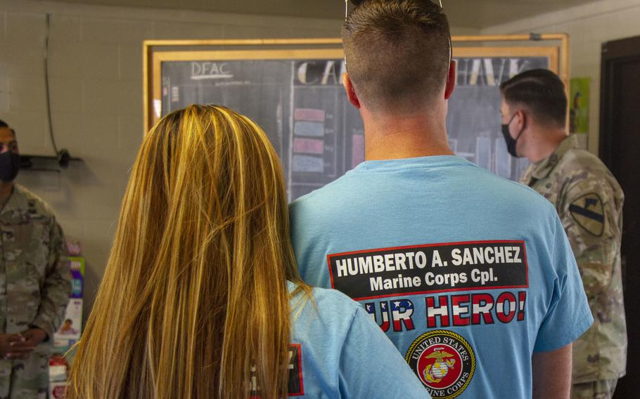 A woman holds her arm around a man, both wearing shirts with their son’s name on it.