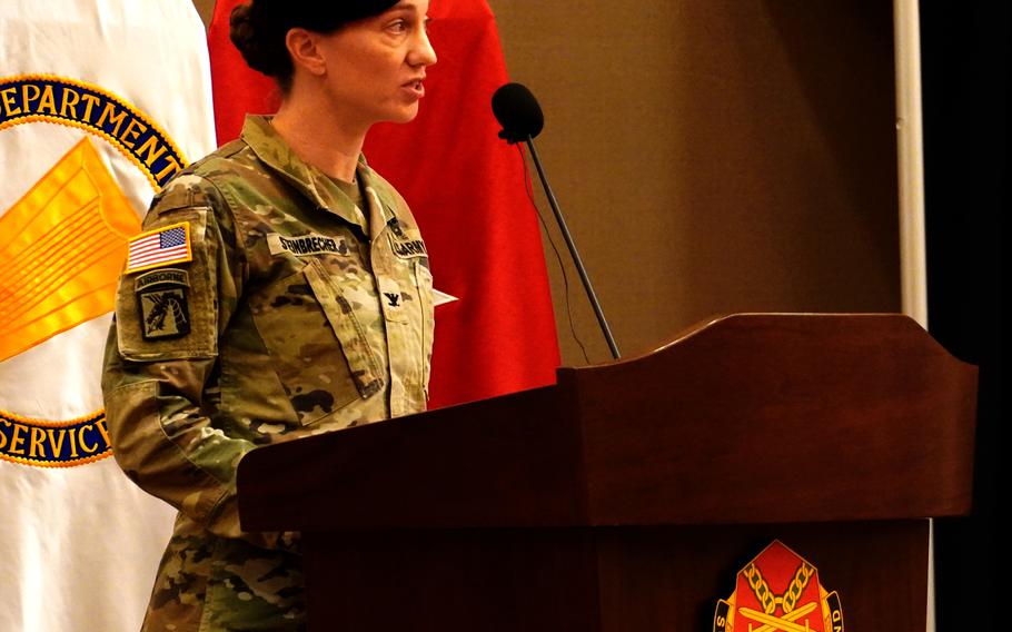 A female U.S. Army soldier speaks at a wooden podium. 