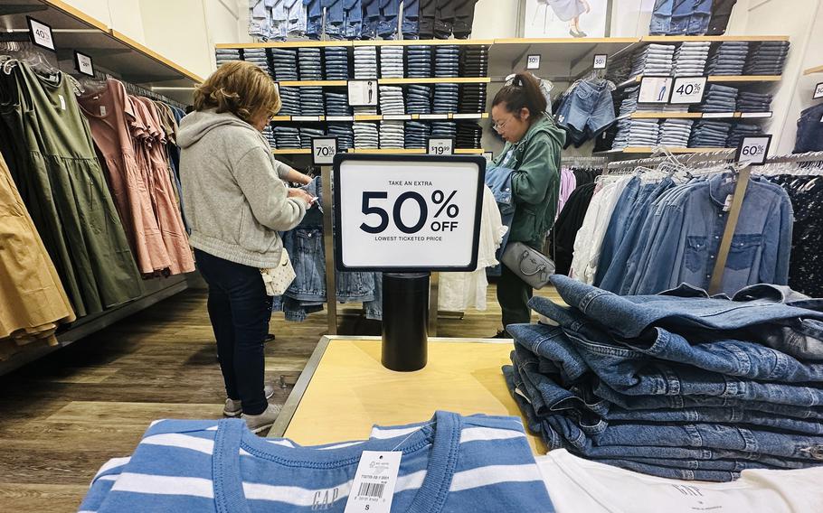 Women shop in a Gap store. A sign between them says 50% off.