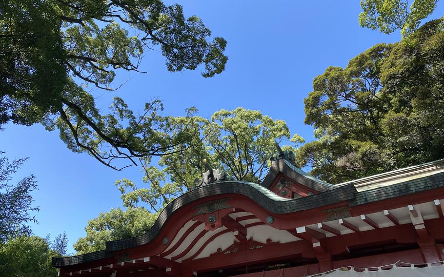 The red roof of a Japanese shrine is seen from below, fringed by trees and blue sky above.