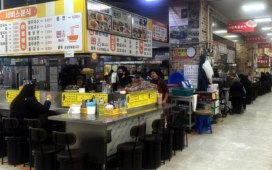 A diner sits at a counter at a food stall in a South Korean market.