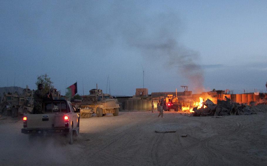 In this April 28, 2011, photo, an Afghan National Army pickup truck passes parked U.S. armored military vehicles, as smoke rises from a fire in a trash burn pit at Forward Operating Base Caferetta Nawzad, Helmand province south of Kabul, Afghanistan. 