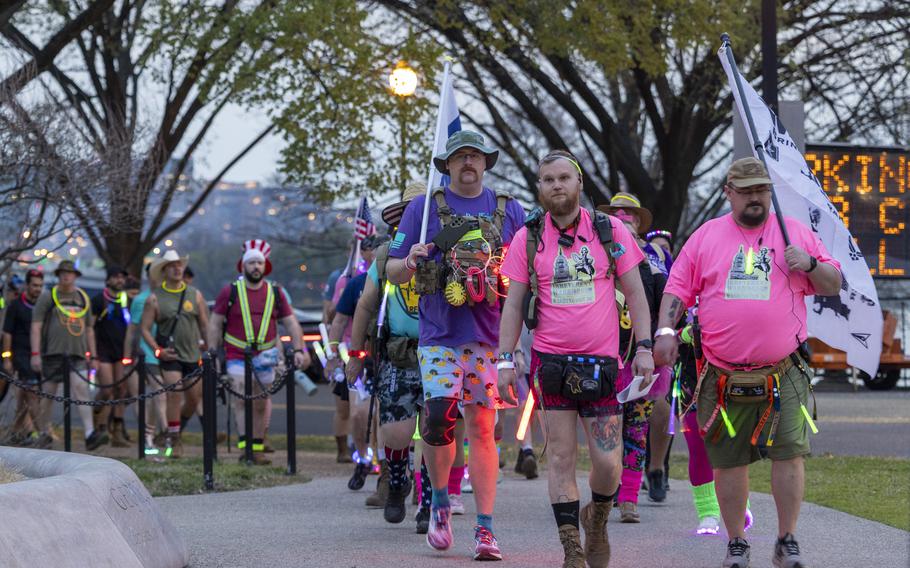People in colorful shirts walk on a sidewalk with a flag