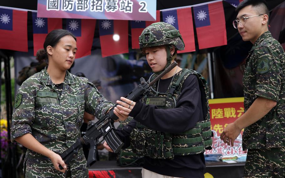 A visitor tries a military outfit and holds a rifle at an army recruiting booth at a pre-National Day street fair, on Oct. 9, 2023, in New Taipei City, Taiwan.