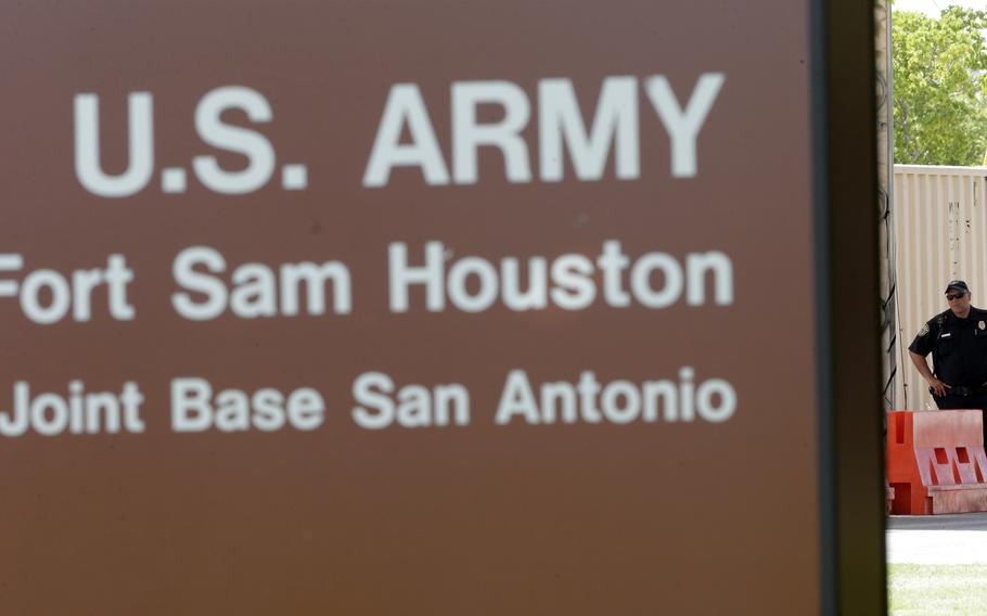 A close-up of a gate for Fort Sam Houston, with a guard in the background.