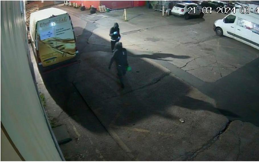 Two people wearing black hoodies and masks are seen from a still from a warehouse’s security camera.