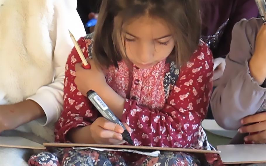 An Afghan girl writes on a whiteboard during an English lesson at Rhine Ordnance Barracks in Kaiserslautern, Germany, Sept. 23, 2021. 