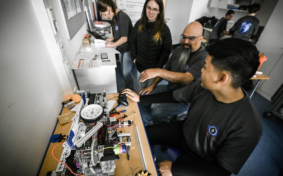 Alfredo Rios, coach of the Ramstein robotics team, at center, gives feedback on a robot's paper airplane launcher to team engineers Gwyn Cedarholm and Deylan Acasio, at Ramstein High School, March 18, 2024. The team is slated to compete at the First Tech Challenge World Championships in April.