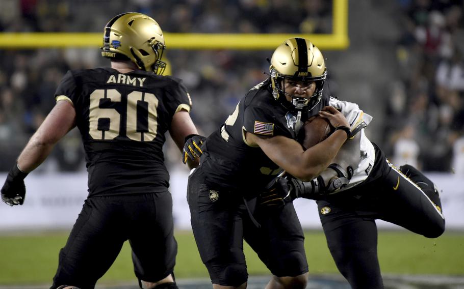 Army’s Connor Finucane (60) looks on as running back Tyson Riley attempts to escape the grasp of Missouri defensive lineman Darius Robinson, right, in the first half of the Armed Forces Bowl NCAA college football game in Fort Worth, Texas, Wednesday, Dec. 22, 2021.