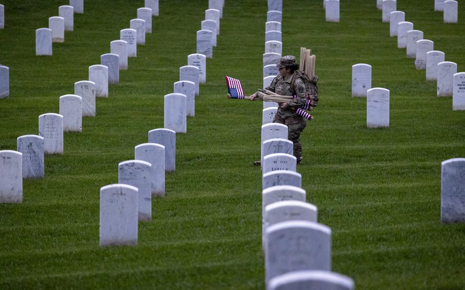 A soldier prepares to place a flag among lines of headstones.
