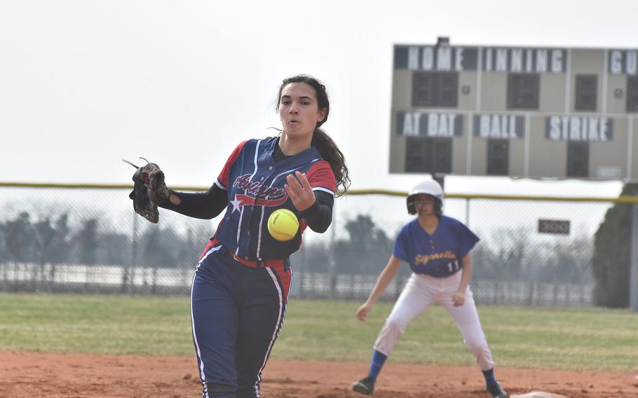 Aviano's Sophia Scavo sends the ball toward the plate while Sigonella baserunner Angeliah Barraza-Hernandez waits in the background during a game Saturday, March 18, 2023, at Aviano Air Base, Italy.