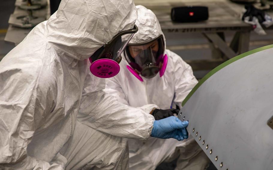 Michael Vallely, left, and Daniel Wondering, assigned to Fleet Readiness Center Southwest, shave titanium grommets on the engine bay door of an F/A-18E Super Hornet aircraft attached to Strike Fighter Squadron 136, aboard the  aircraft carrier USS George H. W. Bush in the Adriatic Sea, Dec. 16, 2022. A Super Hornet damaged by an engine fire in August should be back in action soon,  the Navy said. 