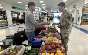 A Korean man hands a small fruit to U.S. airman. 