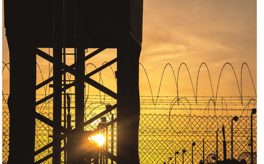The sun rises behind a tower and fence.