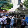 Spectators watch and take pictures of a tank driving down a street.
