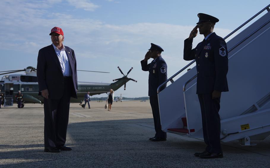President Donald Trump in a suit and red hat looking to the side as he stands in front of the steps of Air Force One.