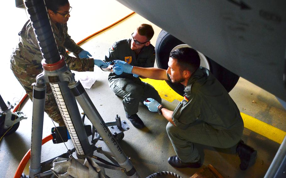 Tech Sgt. Hazel Cochran, left, hands safety goggles to German military academy cadet Tom Palzer before he and fellow cadet Tim Herbst, center, change the tires on a C-130J at Ramstein Air Base on July 15, 2021. The future Luftwaffe pilots are the first from the German military academy to train with U.S. Air Force maintenance crews at Ramstein Air Base.