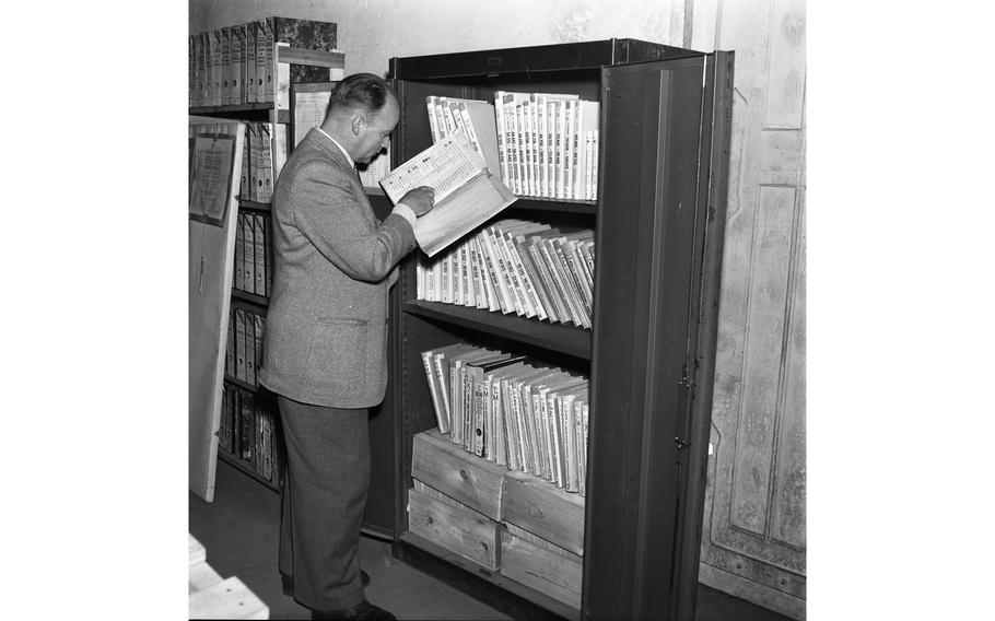 An investigator searches through the entry registers of the Dachau concentration camp in the records room of the International Tracing Service.