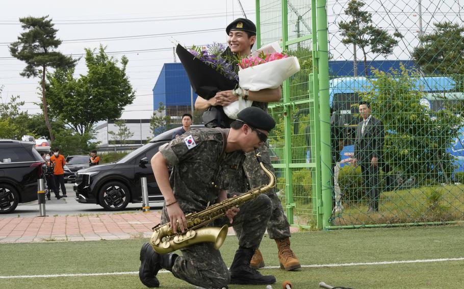 One man in fatigues holding flowers and another man playing the saxophone.