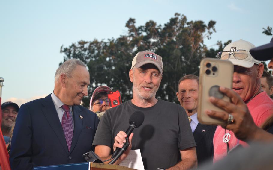 Comedian Jon Stewart speaks at a news conference Tuesday, Aug. 2, 2022, following the Senate approval of the PACT Act — legislation that will expand eligibility for health care and benefits for veterans exposed to burn pits and other toxins. Senate Majority Leader Chuck Schumer, D-N.Y., and Sen. Richard Blumenthal, D-Conn., are standing behind Stewart.