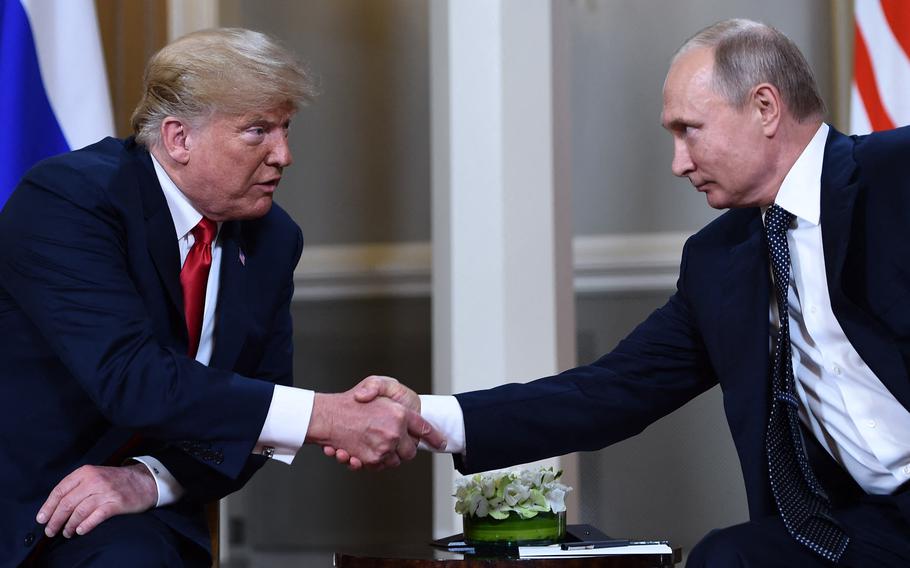 Donald Trump and Vladimir Putin lean towards each other and shake hands while seated next to each other.