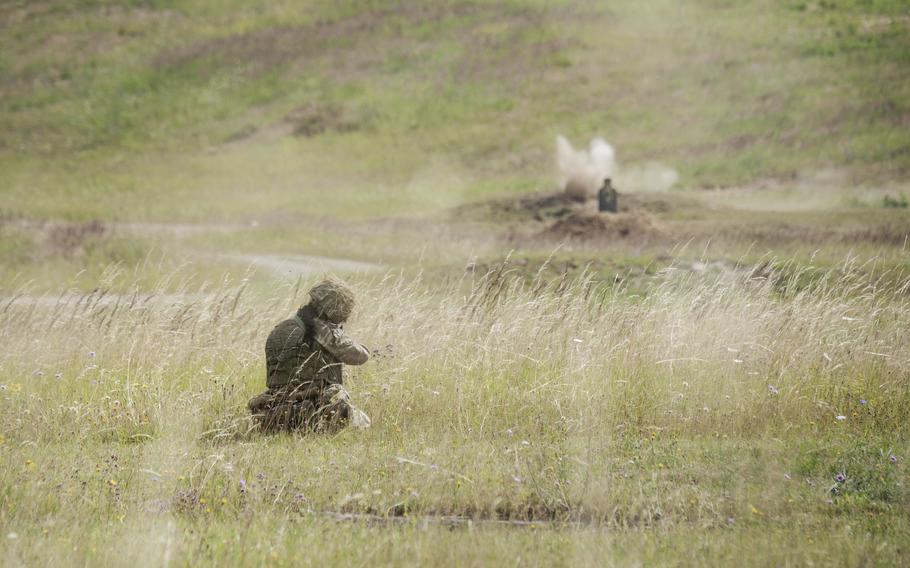 A British cadet crouches in tall grass during a live-fire drill. 