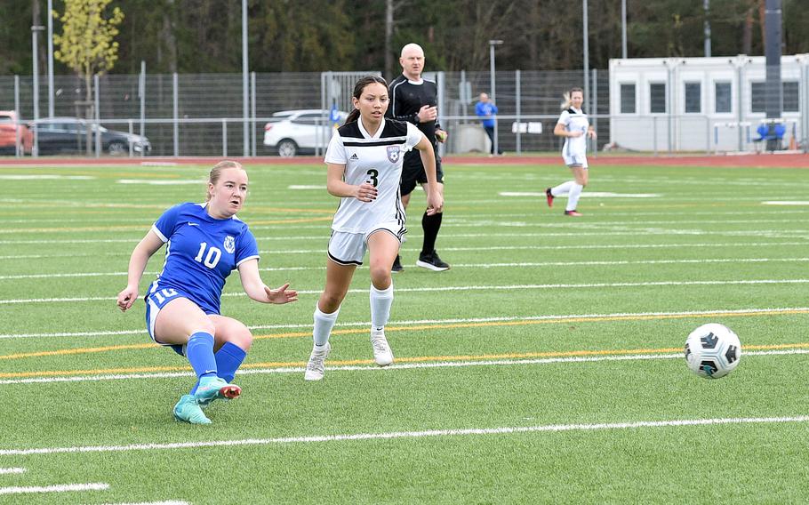 Ramstein striker Claire Boynton follows her shot as SHAPE center back Olivia Penry trails the play during a match on April 5, 2024, at Ramstein High School on Ramstein Air Base, Germany.