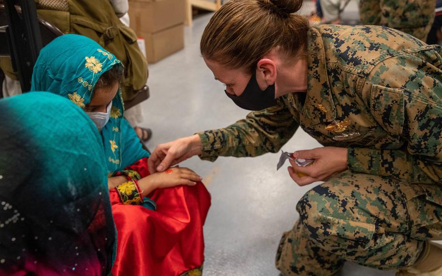 Navy Lt. Cmdr. Julie Anderson hands out stickers to Afghan evacuees preparing to get their coronavirus vaccine booster shots in Upshur Village at Marine Corps Base Quantico, Va., on Dec. 9, 2021. 