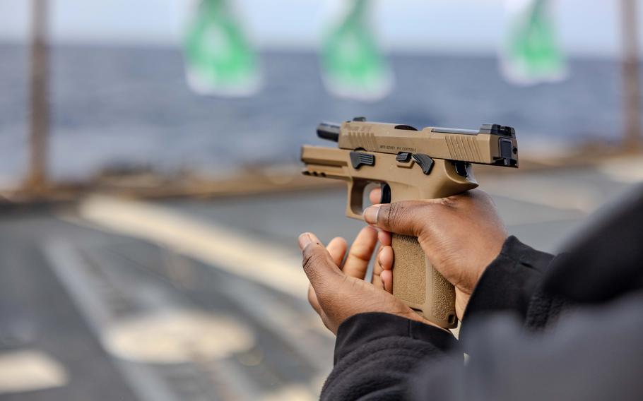 A service member’s arms and hands are shown holding and firing a pistol.