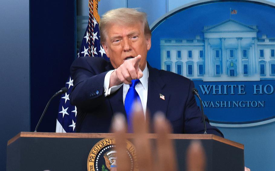 Donald Trump stands at a podium in front of a U.S. flag and the seal of the White House and points in front of him to reporters raising their hands at a press conference.