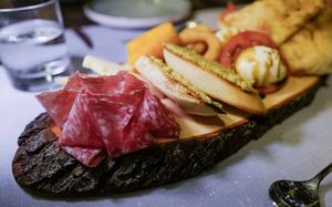 An appetizer platter of cold-cut salami, croquettes, fried onion rings and tomato mozzarella drizzled in balsamic vinegar is served on a rustic wooden board at Grifo Restaurant in Kerzenheim, Germany.