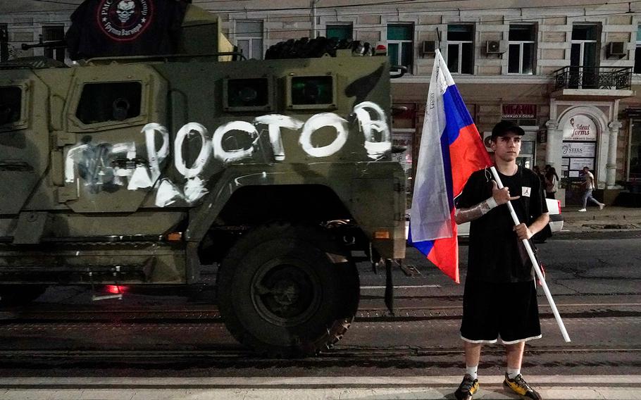 A man holds the Russian national flag in front of a Wagner group military vehicle with a sign reading “Rostov” in Rostov-on-Don, June 24, 2023. Rebel mercenary leader Yevgeny Prigozhin who sent his fighters to topple the military leaders in Moscow will leave for Belarus and a criminal case against him will be dropped as part of a deal to avoid “bloodshed,” the Kremlin said on June 24.