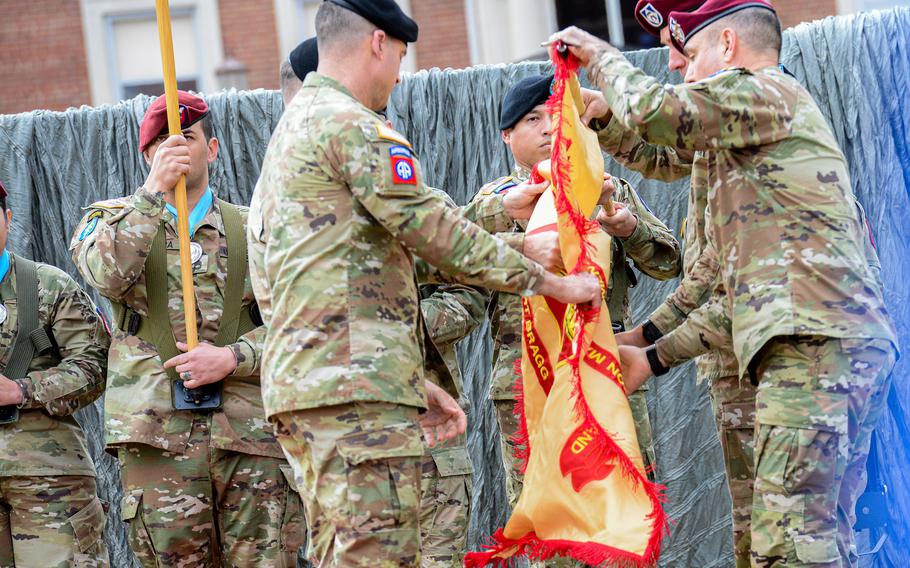 Soldiers fold a flag as other soldiers stand in the back holding other flags.